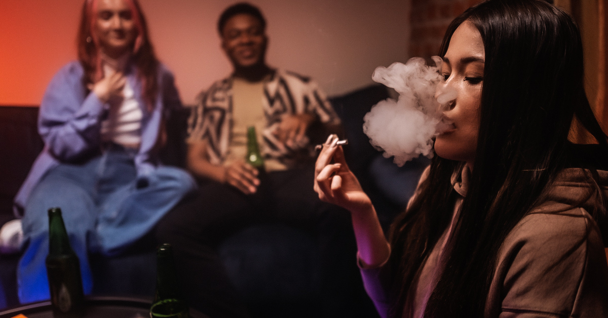 A hand holding a glass of alcohol and a marijuana joint