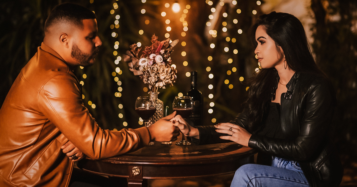 Two glasses of red wine being clinked together on a table full of candles and roses.